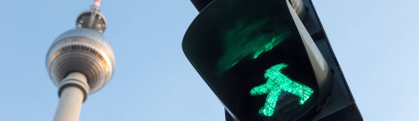 Blick auf Verkehrsampel mit grünem Ampelmännchen, im Hintergrund der Berliner Fernsehturm.