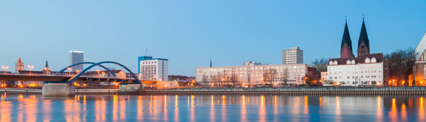 Blick auf die Oderbrücke in Frankfurt (Oder) in den Abendstunden von der polnischen Seite aus. Im Vordergrund die Oder, dahinter die Brücke und die Skyline mit Oderturm.