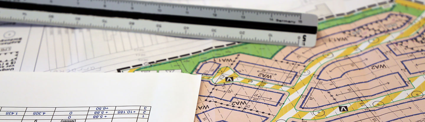 Das Foto zeigt die Planzeichnung eines Bebauungsplans, auf dem ein Textdokument und ein Maßstab liegen.