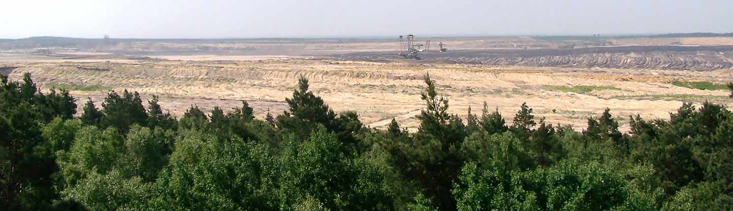 Die Abbildung zeigt den Braunkohlentagebau Welzow in der Lausitz. Der Blick geht über den bereits ausgekohlten und in der Sanierung befindlichen Bereich in Richtung Tagbebaugrube. In der Mitte des Bildes ist schweres Großgerät zu sehen, welches Sanierungsmaßnahmen durchführt.