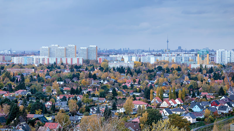 Blick auf die Hochhauskulisse des Berliner Bezirks Marzahn-Hellersdorf. Im Vordergrund befinden sich Einfamilienhäuser. Im Hintergrund ist der Berliner Fernsehturm zu erkennen.